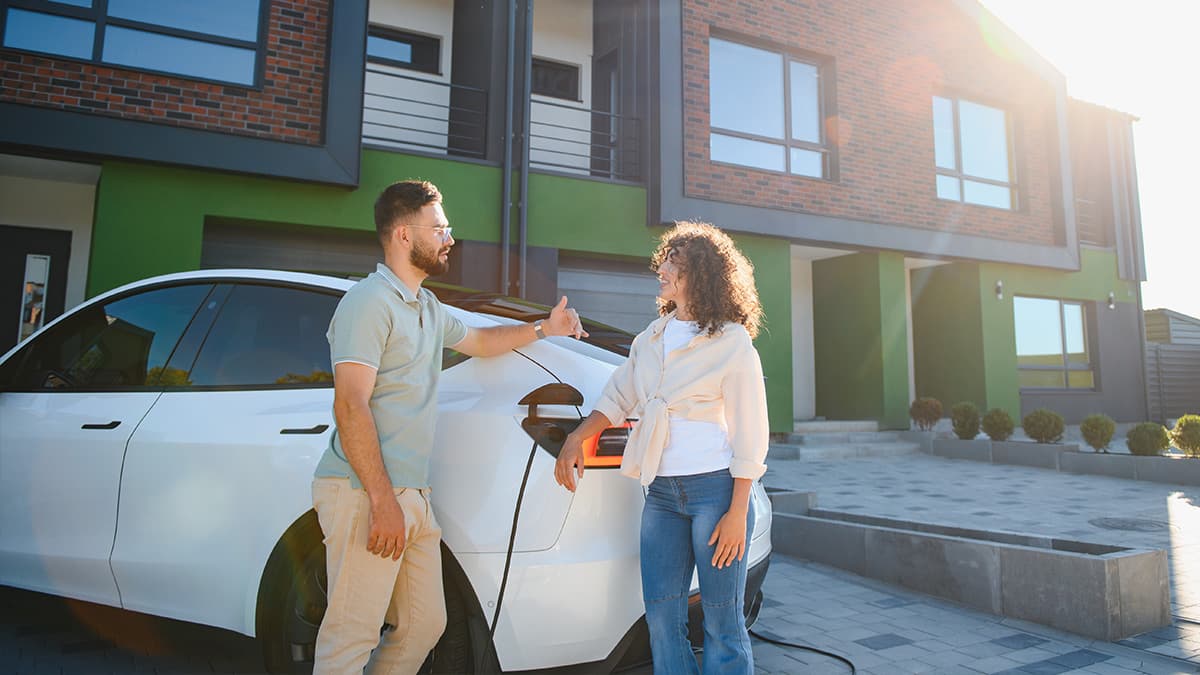 home-ev-charger-installation-cost-pacific-palisades-og Homeowners charging an electric vehicle outside a modern home, illustrating EV charger installation cost in Pacific Palisades