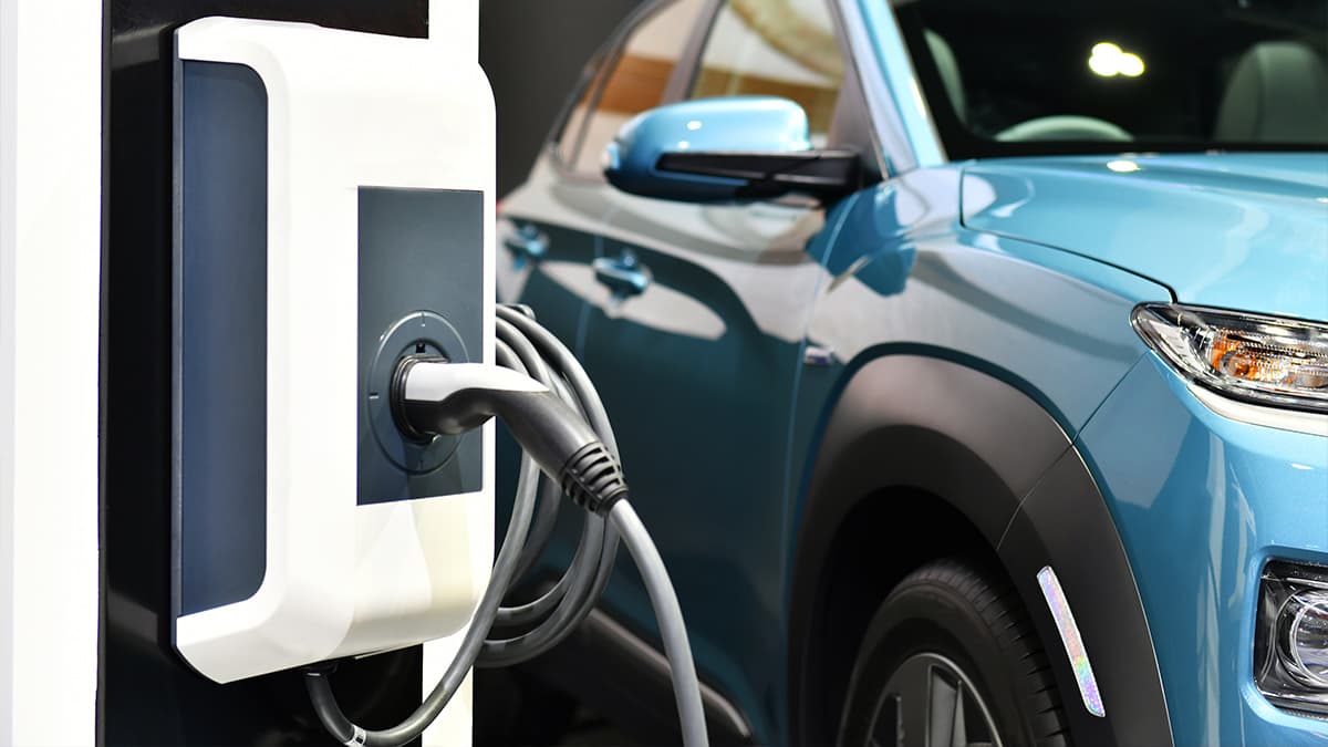 electrical-panel-level-2-ev-charger-los-angeles-og Wall-mounted EV charger beside a blue electric vehicle, illustrating home charging options in Los Angeles.